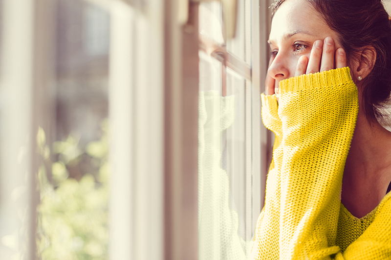 woman in yellow jumper looking out of window