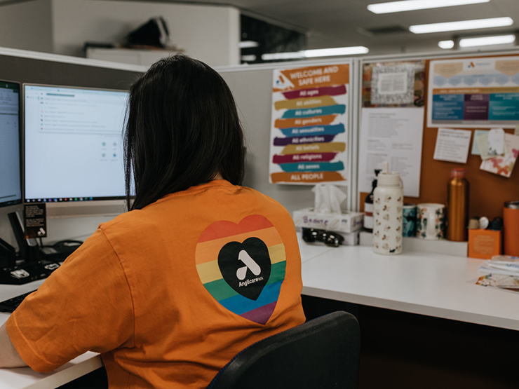 An image of a lady's who is sitting looking at her computer screen wearing an Anglicare WA shirt.