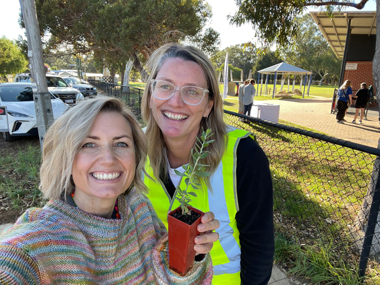 Two females taking a selfie smiling at the camera with a plant in their hand