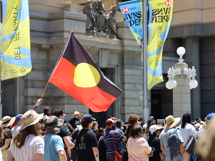 A large Aboriginal flag waving above in a crowd of people 