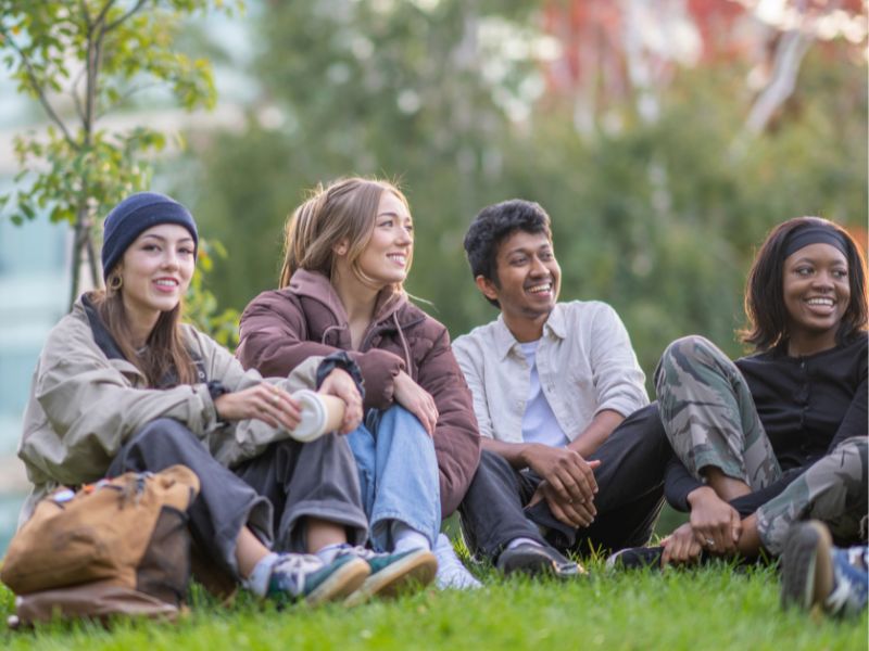 A group of young adult friends sitting on the grass during golden hour.