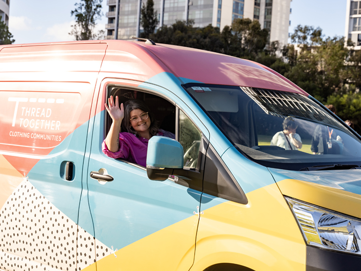 A Thread Together worker waving from the front seat of the bright and colourful thread together van.