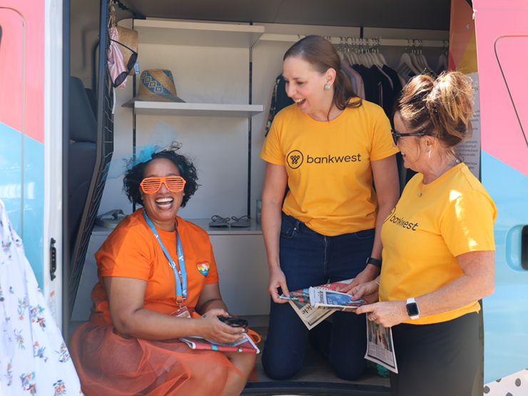 Two people standing and one person sitting in the side of a van laughing.