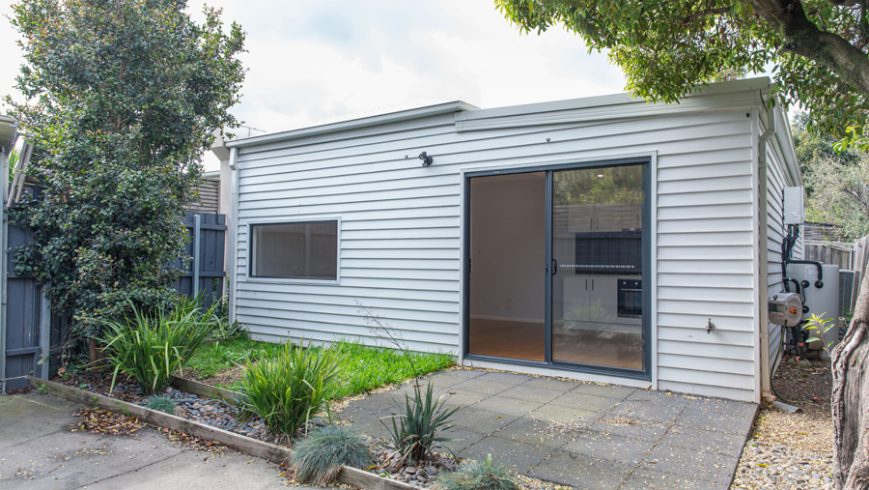A white weatherboard granny flat in an Australian backyard.