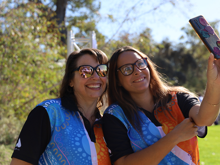 Two females wearing Anglicare WA shirts with Aboriginal designs on them taking a selfie