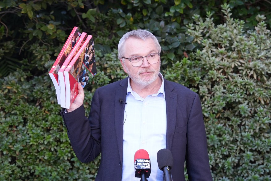 Anglicare WA CEO Mark Glasson holding up three volumes of the State Budget papers