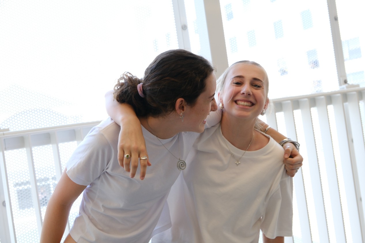 A photo of two high school aged friends smiling with arms around each other's shoulders.