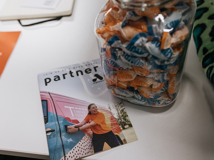 Image of a booklet that has the title 'Join us as Meaningful Partner' written on the front. The booklet is resting on a white table with lollies in a jar next to it.