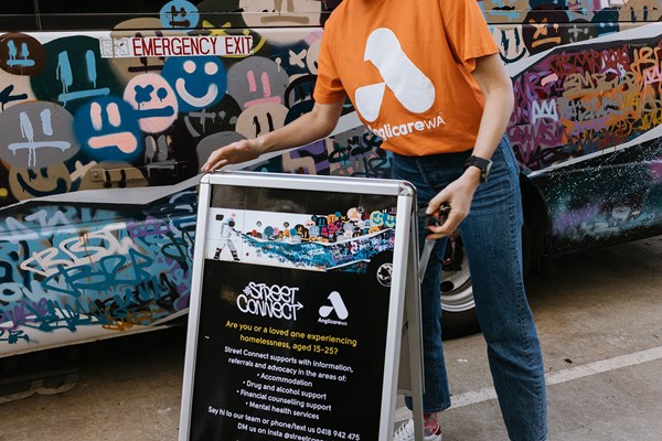An Anglicare WA worker placing an A-frame sign for Street Connect Services.