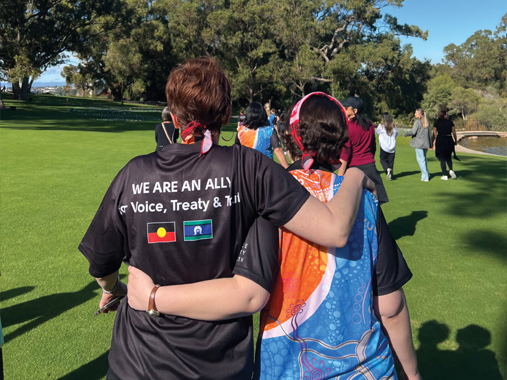 Image of two peoples backs who are walking, they are wearing Anglicare WA shirts with Aboriginal artwork on them.