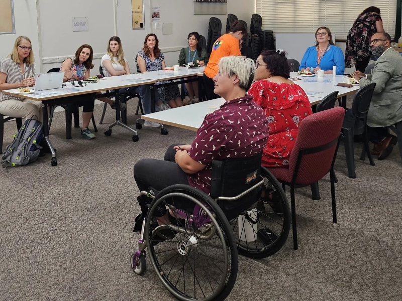 A group of individuals around table at a meeting, including person in wheelchair