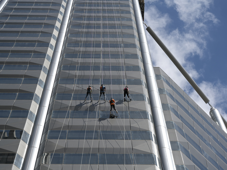 Four people in orange abseiling off the side of a building. They are half way down with the picture taken from the ground looking up.