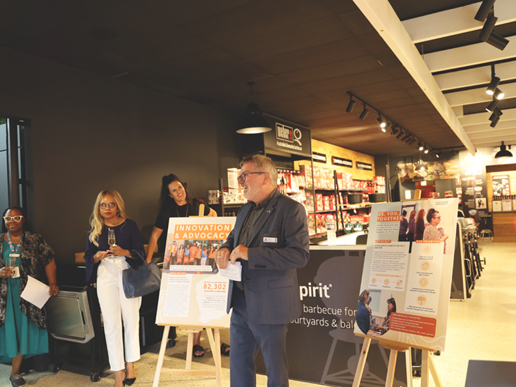 CEO Mark Glasson talking to a group in front of several graphically designed boards with Anglicare WAs advocacy priorities written on them