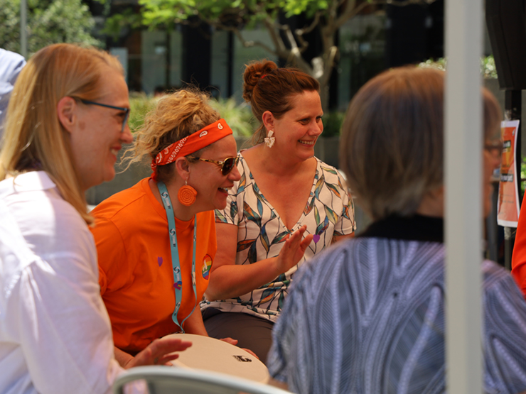A group of Anglicare WA employees who are sitting outside and smiling and laughing at something out of shot.