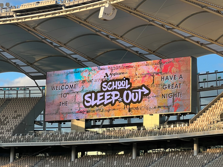Image of a sports stadium with a graphic on a screen above seats that says 'Welcome to the School Sleep Out Have a Great Night'.