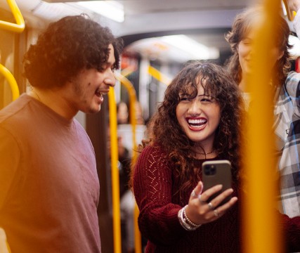 Group of friends on the train happily discussing something on the phone screen.