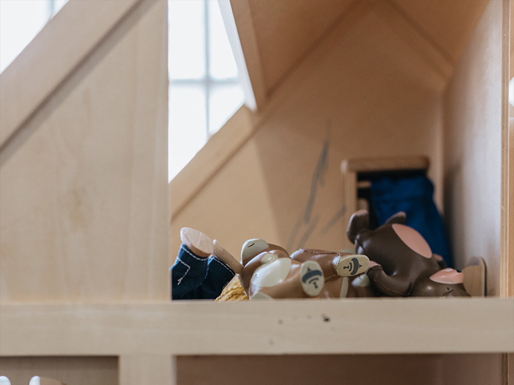 Close up shot through a window of a dolls house that has a bed and dolls in it that are messily placed