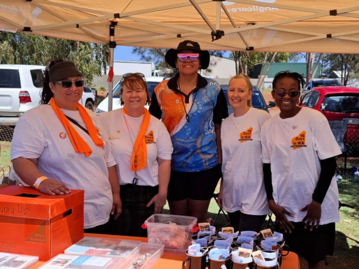 A group of 5 Anglicare WA workers standing under a tent at a community event. They are smiling at the camera.