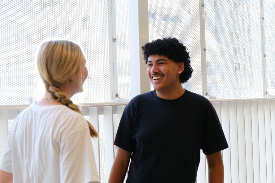 Two high school students smiling and talking in a light and airy undercover walkway. 