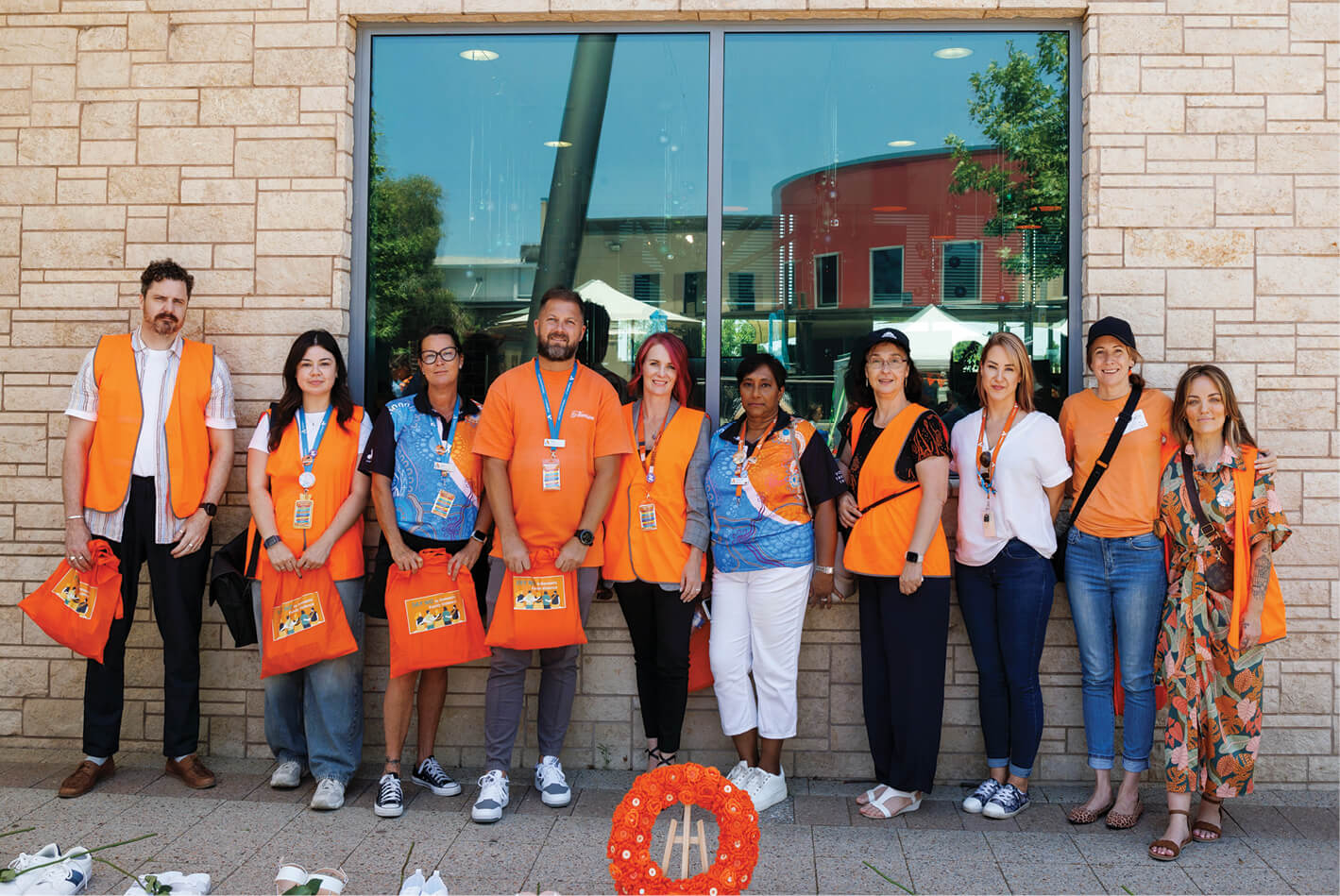 A group of Anglicare WA workers dressed brightly in orange standing outside of Mary Davies Library and Community Centre as part of Rockingham's 16 Days in WA community event.