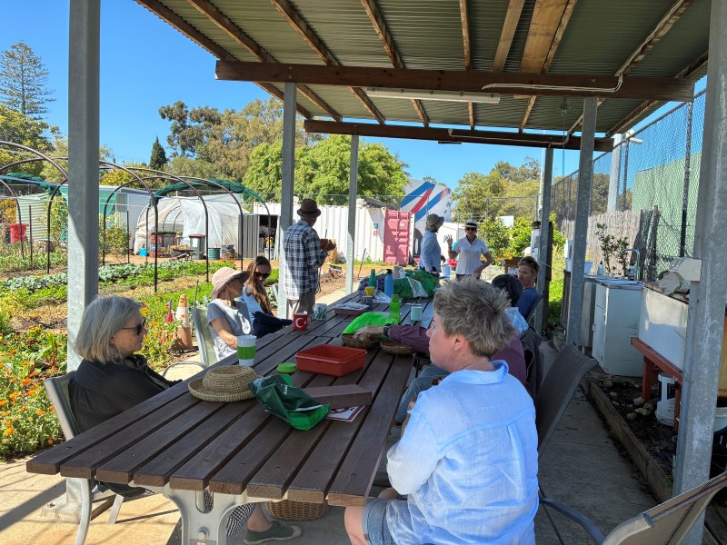 Community members resting around a picnic table overlooking vibrant garden beds.