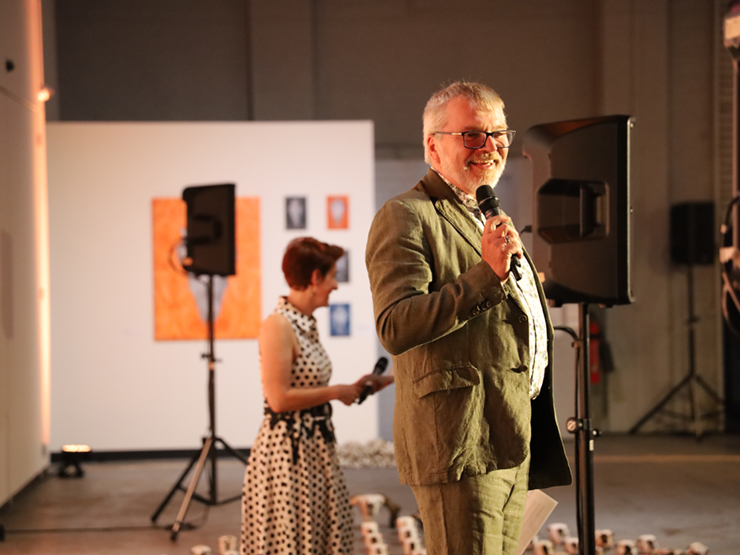 An image of CEO Mark Glasson standing smiling and talking to a crowd with a microphone.