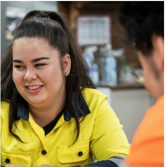 A photo of worker in high vis clothing talking to another worker in breakroom. 
