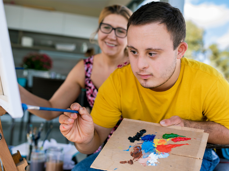 A man paints alongside a woman, both focused on their artwork in a bright, creative environment