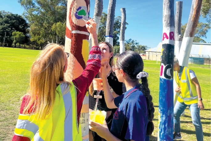 Students and volunteers painting a decorative timber pole together. 