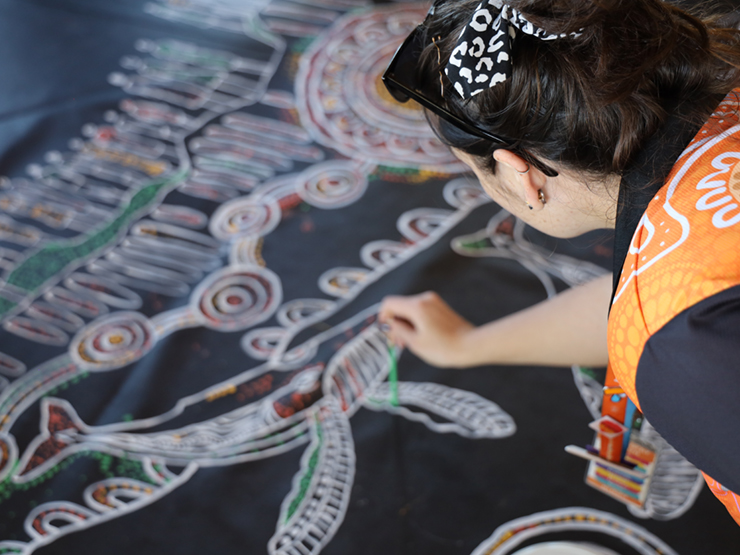 Anglicare WA worker painting on a large canvas which is laid out on the ground.