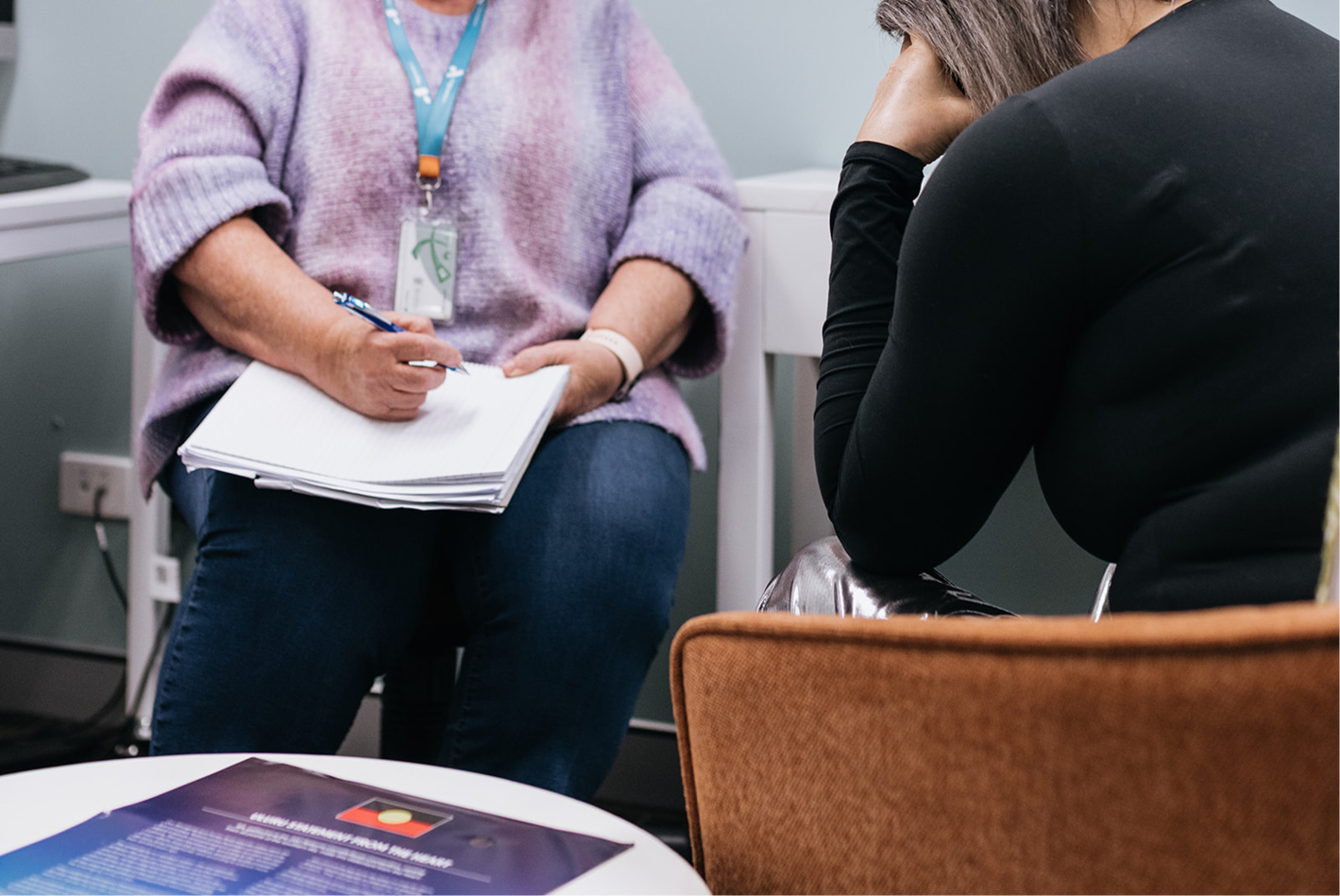 A person sitting with a notepad writing as another person sits talking to them.