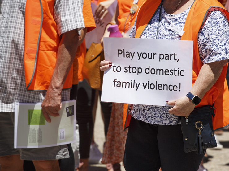 Older couple walking with a group holding a sign that says, 'Play your part, to stop domestic and family violence!'