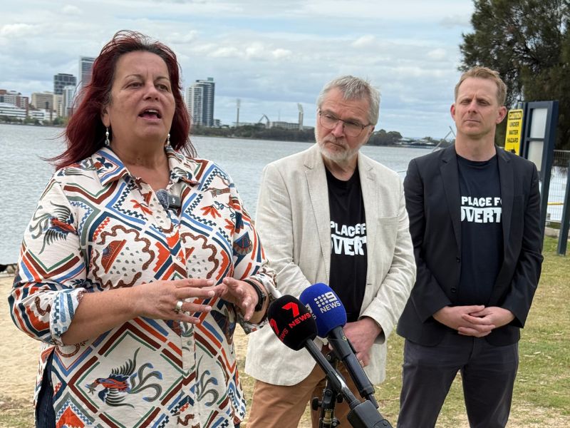 Three spokespeople speaking into microphones on the riverside at the announcement of the 2026 Poverty Snapshot.